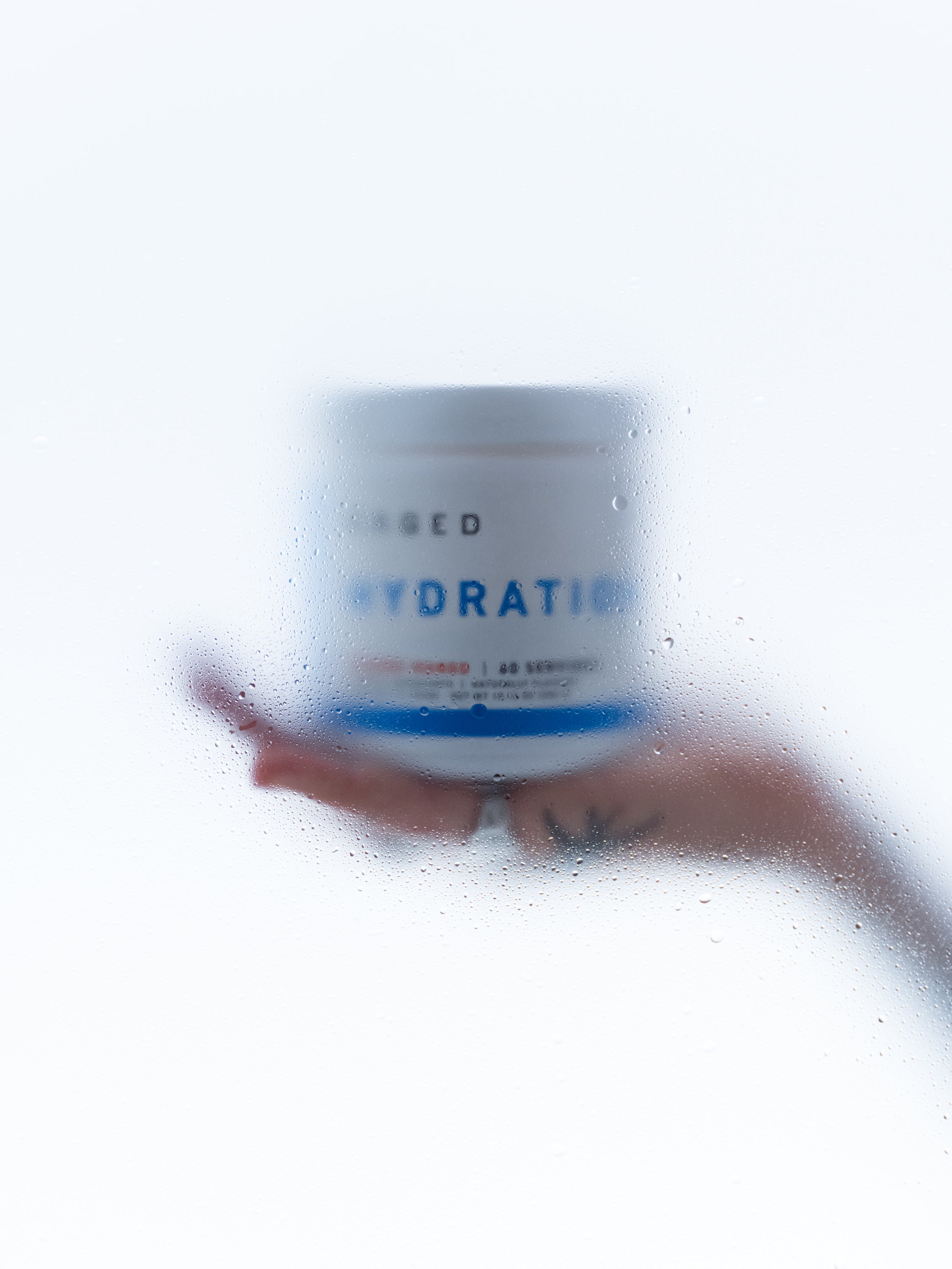 Front view of KAGED Hydration tub held on a hand showcasing the HYDRATION label behind misted glass