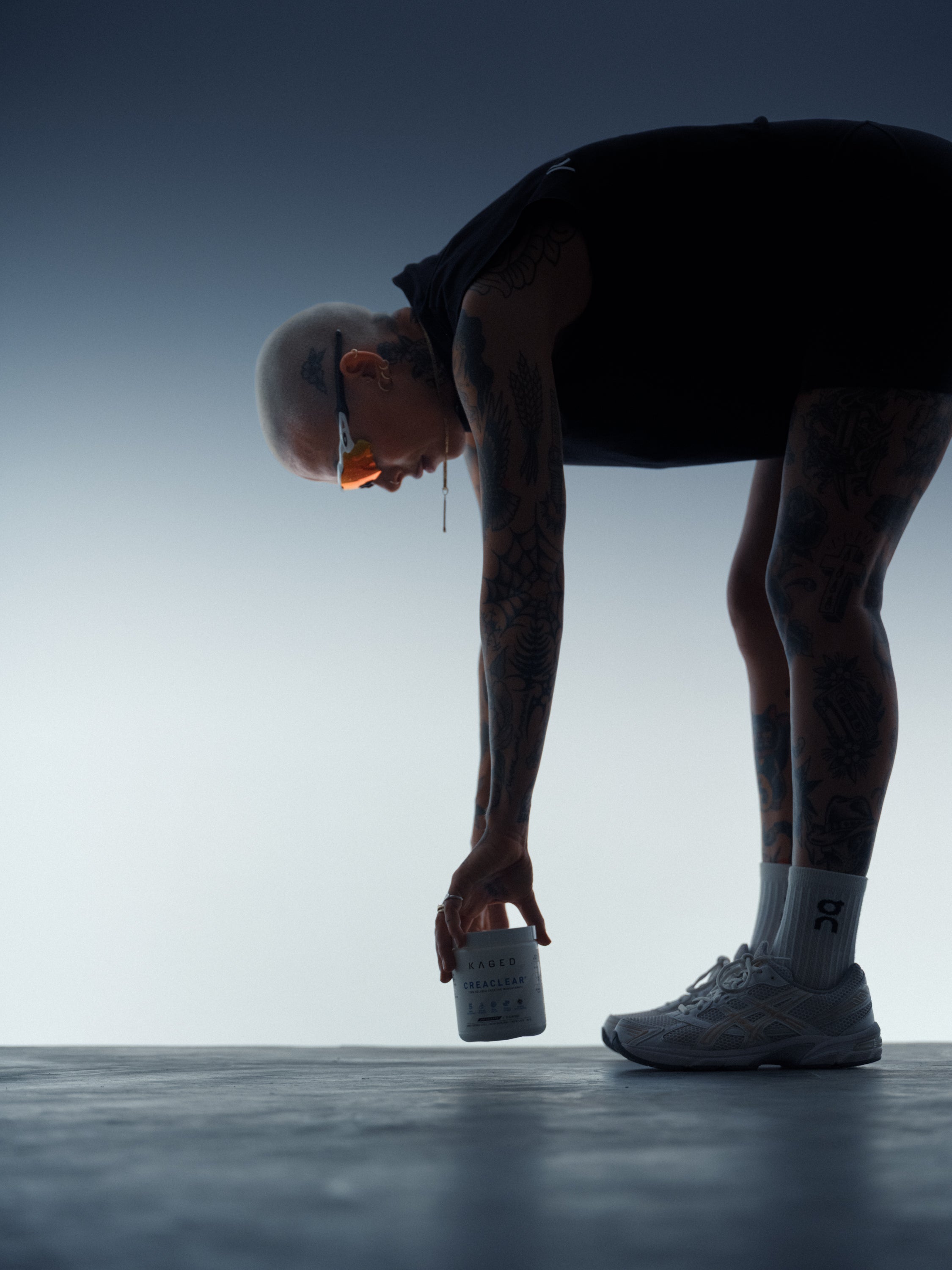 Side view of a KAGED supplement tub being placed on a backlit studio floor by an athlete